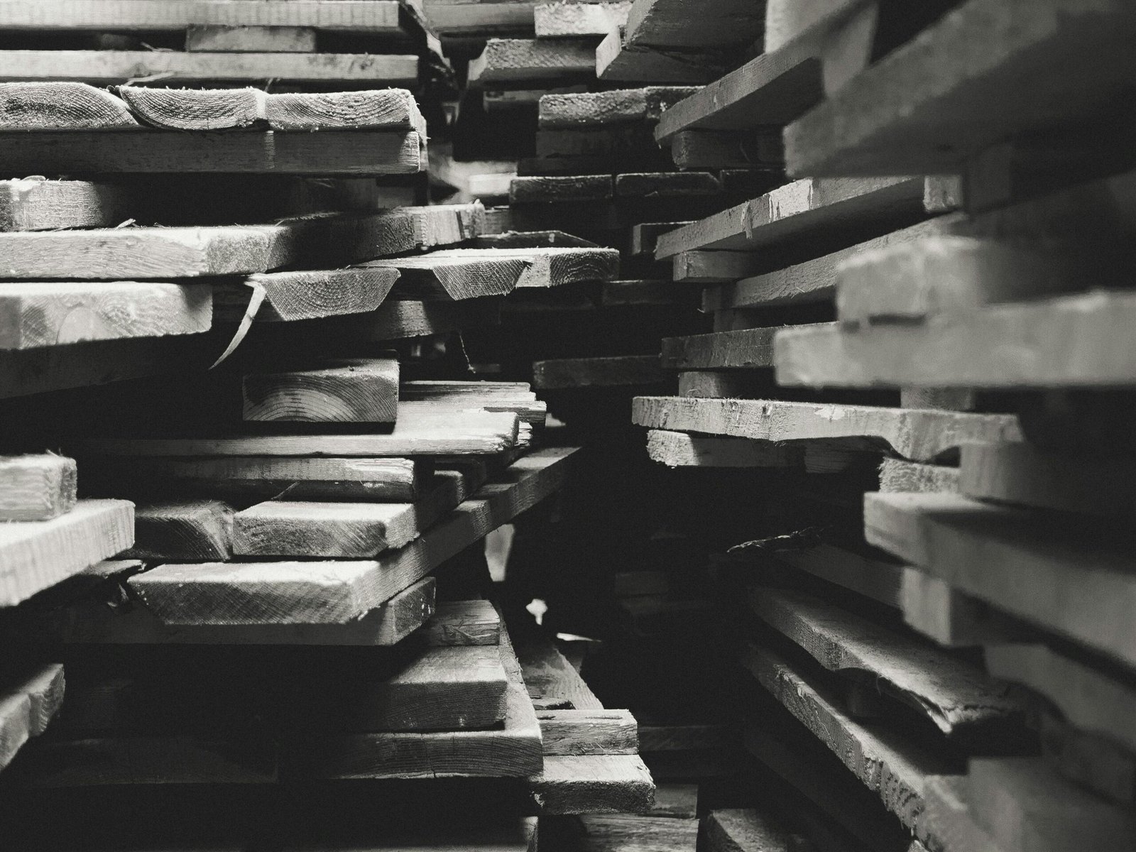Unique Wood Cutting Boards & Furniture Made for your Home Artistic black and white photograph of stacked lumber in a warehouse setting.